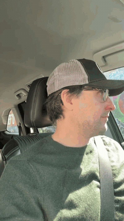 A Man Wearing Glasses And A Hat Is Sitting In A Car GIF