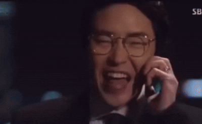 A Man Wearing Glasses And A Hat Is Smiling While Talking On A Cell Phone GIF