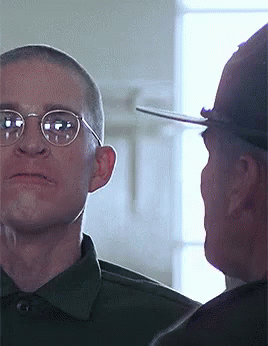 A Man Wearing Glasses And A Hat Looks At Another Man GIF