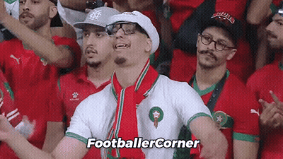 A Man Wearing Glasses And A Hat Stands In A Crowd Of People And Says Footballercorner GIF