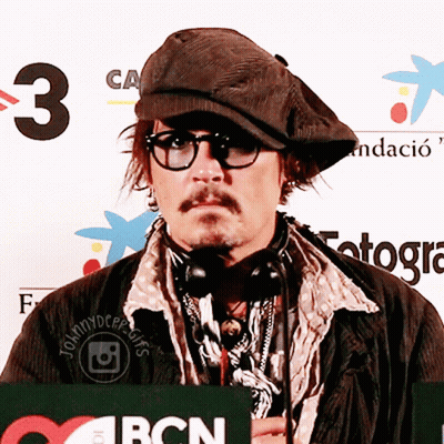 A Man Wearing Glasses And A Hat Stands In Front Of A Bcn Sign GIF