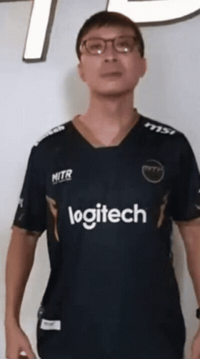 A Man Wearing Glasses And A Logitech Shirt Stands In Front Of A White Wall GIF
