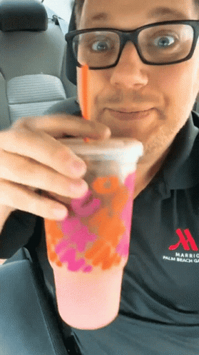 A Man Wearing Glasses And A Marriott Shirt Drinks A Pink Drink GIF