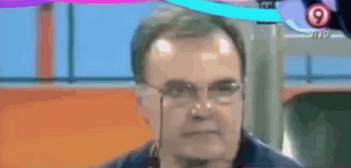 A Man Wearing Glasses And A Medal Around His Neck Is Talking On A Tv Screen . GIF