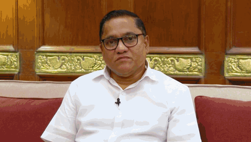 A Man Wearing Glasses And A Microphone Sits On A Red Couch GIF