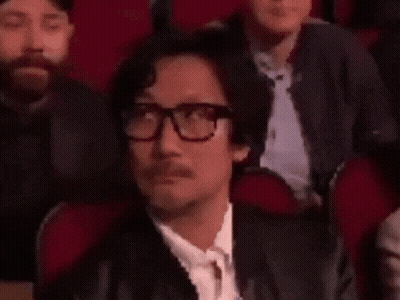 A Man Wearing Glasses And A Mustache Is Sitting In A Theatre . GIF