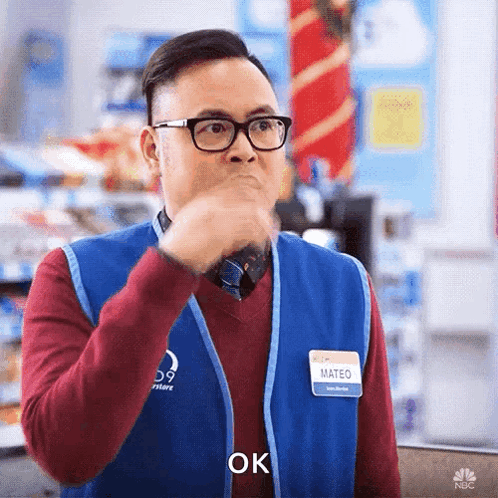 A Man Wearing Glasses And A Name Tag That Says Mateo Is Holding His Hand To His Mouth And Saying Ok . GIF