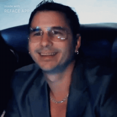 a man wearing glasses and a necklace is smiling in a video made with reface app