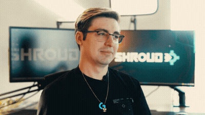 A Man Wearing Glasses And A Necklace Stands In Front Of A Screen That Says Shroud GIF