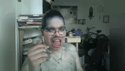 A Man Wearing Glasses And A Necklace With The Letter G On It Is Smoking GIF
