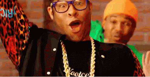 A Man Wearing Glasses And A Necklace With The Word Kooice On It . GIF
