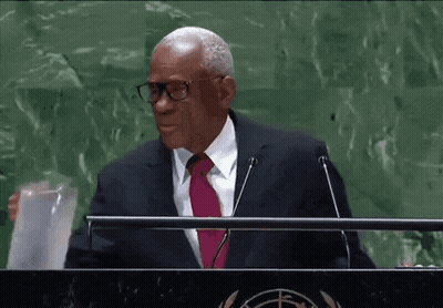 A Man Wearing Glasses And A Pink Tie Stands At A Podium GIF