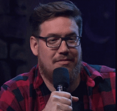 A Man Wearing Glasses And A Plaid Shirt Is Holding A Microphone . GIF