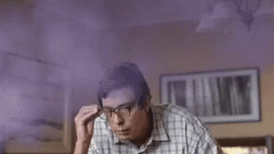 A Man Wearing Glasses And A Plaid Shirt Is Sitting In A Room With Purple Smoke Coming From His Head . GIF