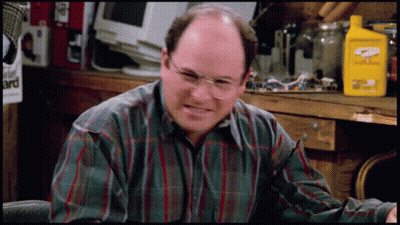 A Man Wearing Glasses And A Plaid Shirt Is Sitting In Front Of A Table With A Yellow Bottle That Says Eagle One GIF
