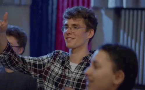 a man wearing glasses and a plaid shirt is smiling and raising his hand in the air