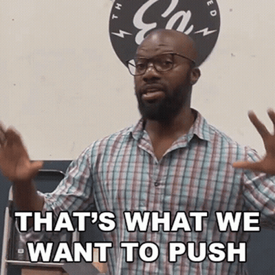 A Man Wearing Glasses And A Plaid Shirt Is Standing In Front Of A Sign That Says That 'S What We Want To Push GIF