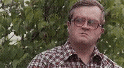A Man Wearing Glasses And A Plaid Shirt Is Standing In Front Of A Tree And Making A Funny Face . GIF
