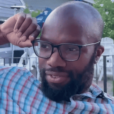 A Man Wearing Glasses And A Plaid Shirt Wipes His Forehead With His Hand GIF