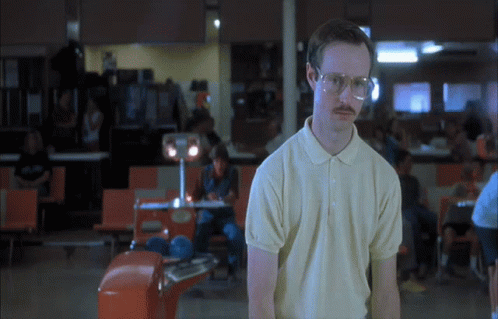 A Man Wearing Glasses And A Polo Shirt Is Standing In A Bowling Alley GIF