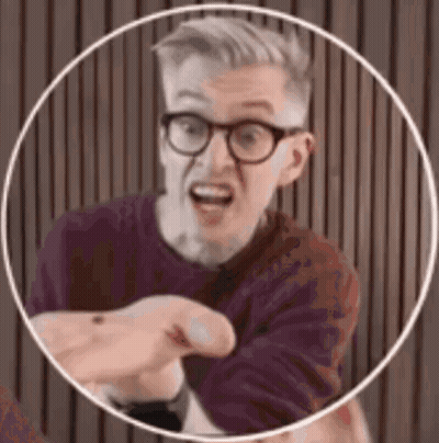 A Man Wearing Glasses And A Purple Shirt Is Pointing At The Camera . GIF