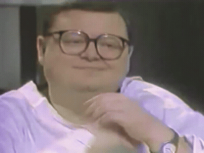A Man Wearing Glasses And A Purple Shirt Is Smiling And Looking At The Camera . GIF