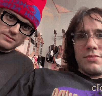 A Man Wearing Glasses And A Red Hat Is Standing Next To Another Man Wearing Glasses And A Hat . GIF