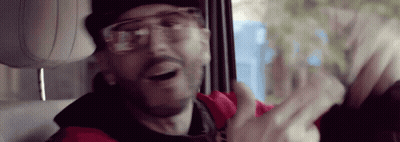A Man Wearing Glasses And A Red Jacket Is Sitting In The Back Seat Of A Car . GIF
