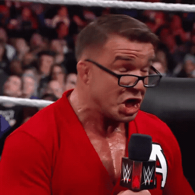 A Man Wearing Glasses And A Red Shirt Is Holding A Microphone And Making A Face . GIF