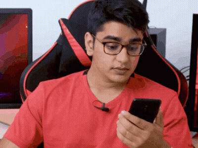 A Man Wearing Glasses And A Red Shirt Is Looking At His Cell Phone GIF