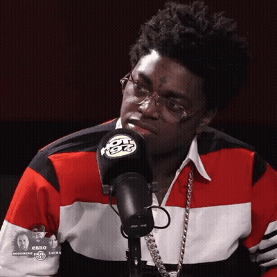 A Man Wearing Glasses And A Red White And Blue Shirt Stands In Front Of A Radio Microphone GIF