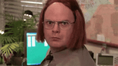 A Man Wearing Glasses And A Red Wig Is Standing In Front Of A Computer Monitor . GIF