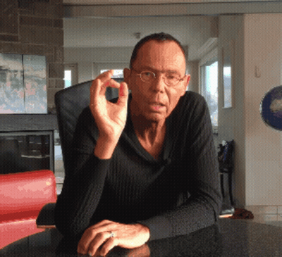 A Man Wearing Glasses And A Ring Sits At A Table With His Hands Folded GIF