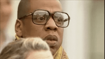 A Man Wearing Glasses And A Scarf Is Looking At Another Man . GIF