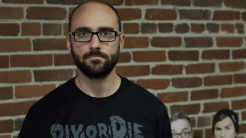 A Man Wearing Glasses And A Shirt That Says Divorce Is Standing In Front Of A Brick Wall GIF