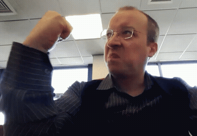 A Man Wearing Glasses And A Striped Shirt Holds His Fist Up In The Air GIF