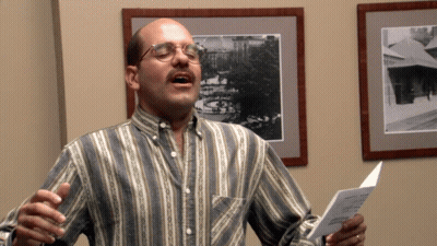 A Man Wearing Glasses And A Striped Shirt Sings Into A Microphone GIF