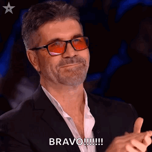 A Man Wearing Glasses And A Suit Is Clapping His Hands And Saying Bravo ! GIF