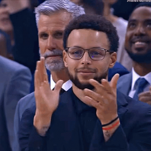 A Man Wearing Glasses And A Suit Is Clapping His Hands In A Crowd Of People . GIF