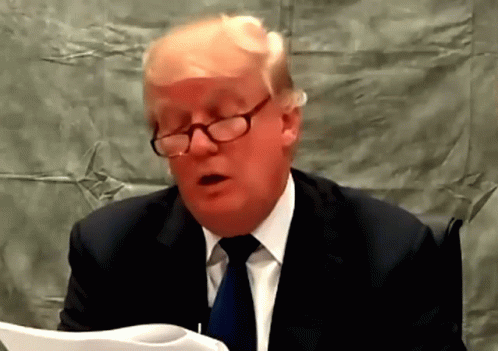 A Man Wearing Glasses And A Suit Is Reading A Paper GIF