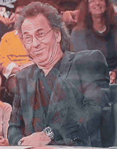 A Man Wearing Glasses And A Suit Is Sitting In A Crowd . GIF