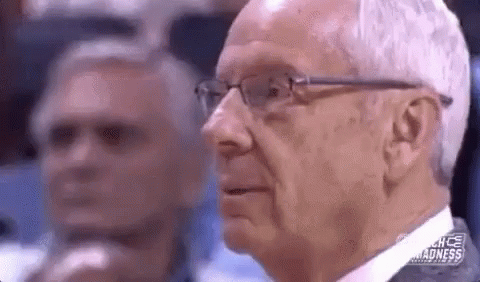 A Man Wearing Glasses And A Suit Is Sitting In A Stadium Watching A Basketball Game . GIF