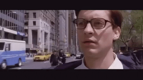 A Man Wearing Glasses And A Suit Is Walking Down A Street . GIF