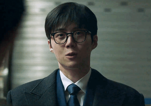 A Man Wearing Glasses And A Suit Looks At The Camera GIF