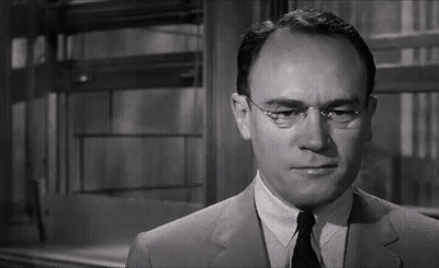 A Man Wearing Glasses And A Suit Looks At The Camera In A Black And White Photo GIF