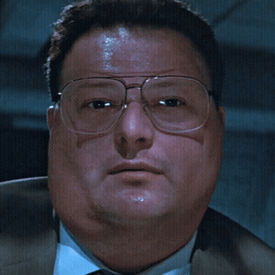A Man Wearing Glasses And A Suit Looks At The Camera With A Serious Look On His Face GIF