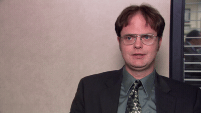 A Man Wearing Glasses And A Suit Stands In Front Of A Wall GIF