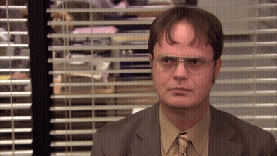 A Man Wearing Glasses And A Suit Stands In Front Of A Window With Blinds GIF