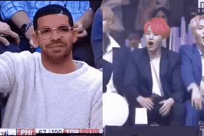 A Man Wearing Glasses And A Sweater Is Sitting In A Stadium Next To A Man With Pink Hair . GIF