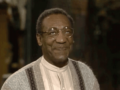 A Man Wearing Glasses And A Sweater Is Smiling And Looking At The Camera . GIF